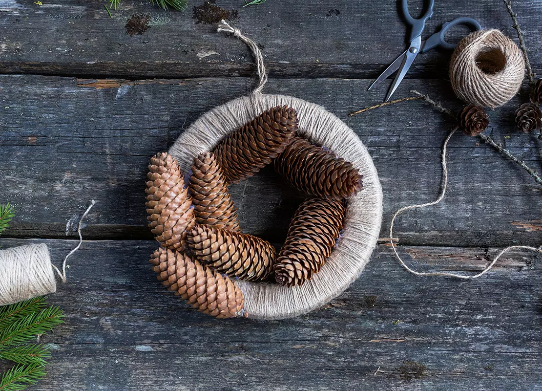 Ein Kranz wird mit Tannenzapfen beklebt. [Foto: AdobeStock_Ali]