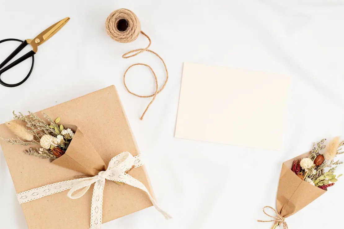 Beige Geschenktüten mit Trockenblumen gefüllt und  geschenkband verziert, Juteschnur und eine Schere daneben arrangiert