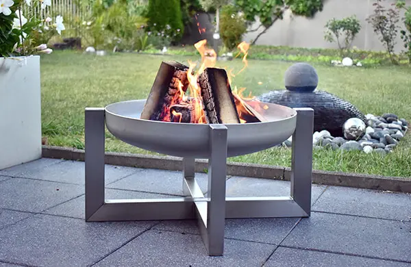 Feuerschale aus Edelstahl mit brennenden Holzscheiten auf einer Terrasse.