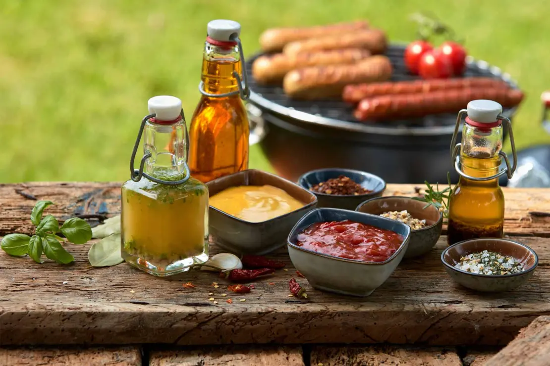 Grillsoßen auf Gartentisch neben Marinaden [Foto: AdobeStock_Exclusive-Design]