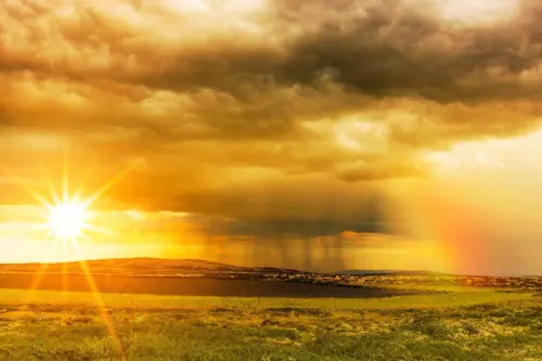 Die scheinende Sonne, eine Regenwolke mit Schauern und ein Regenbogen vor einem goldenen Himmel, auß0erdem ein See und Wiesen