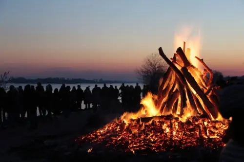 Das Osterfeuer am Strand von Hamburg-Blankenese brennt in der Dämmerung und ist umringt von einer großen Menschenschar, die im Gegenlicht nur in Umrissen zu erkenne ist