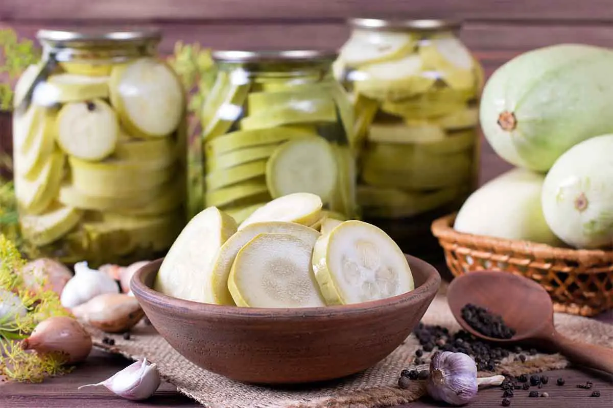 Eingelegte Zucchini in Einmachgläsern und frisch geschnittene Zucchinischeiben in einer Schüssel im Vordergrund – ideal für Zucchinisalat oder als Vorrat für den Winter. [Foto: AdobeStock_qwartm]