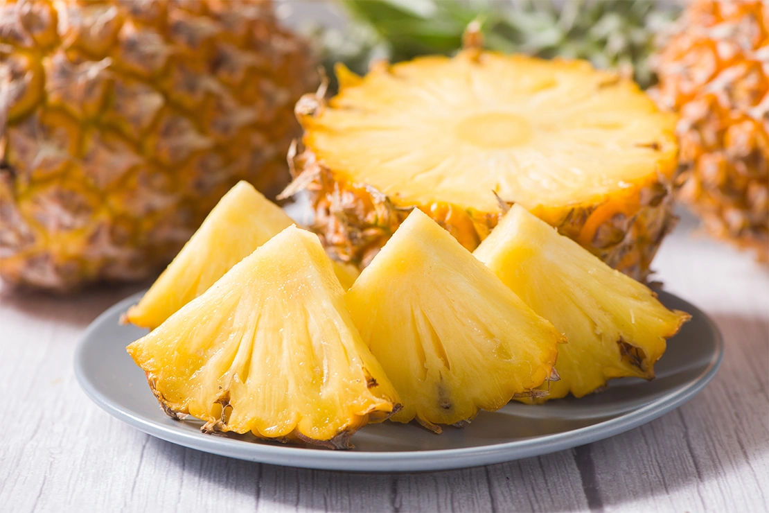 Aufgeschnittene Ananas auf einem kleinen Teller serviert. Im Hintergrund zu sehen ist eine ganze Ananas. Foto: AdobeStock_zhikun sun