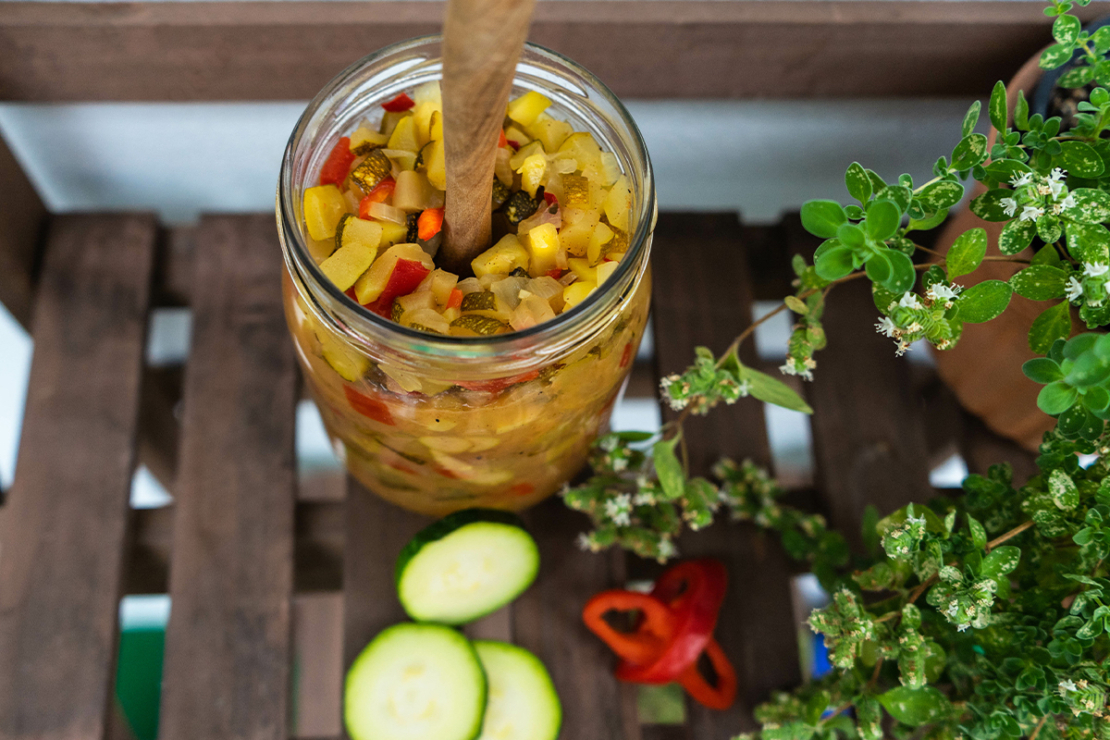 Zucchini-Chutney in einem Glas neben Scheiben und Chili [Foto: AdobeStock_Jana Lösch]