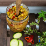Zucchini-Chutney in einem Glas neben Scheiben und Chili [Foto: AdobeStock_Jana Lösch]