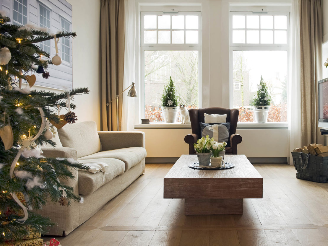 ein Wohnzimmer mit zwei Weihnachtsbäumchen auf der Fensterbank und einem geschmückten Weihnachtsbaum