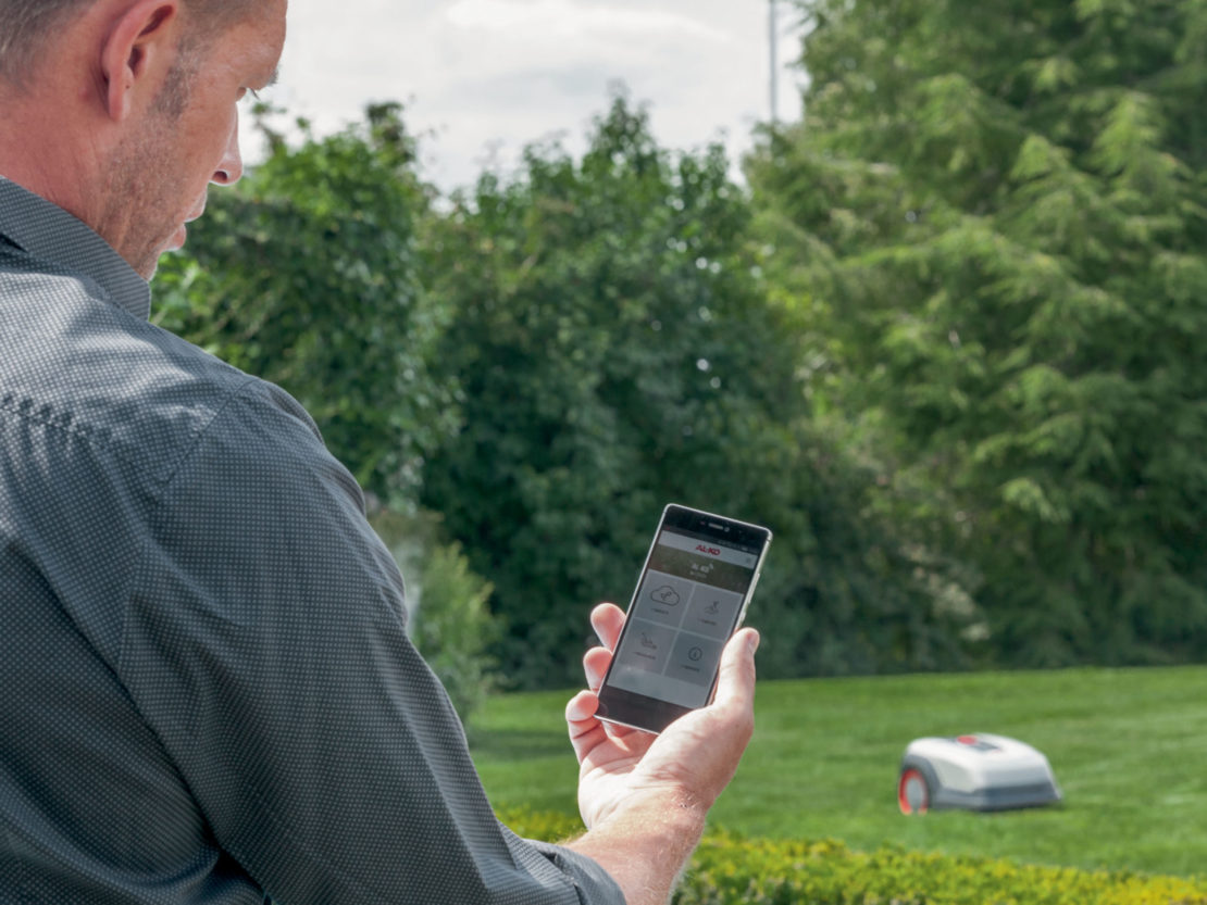 Ein Mann steuert einen Mähroboter vom Smartphone aus.