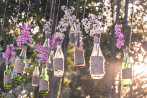 Hängevasen selber basteln – hier hängen mit Kordeln umwickelte Glasflaschen mit Blumen an einer Girlande [Foto: AdobeStock_dimch]