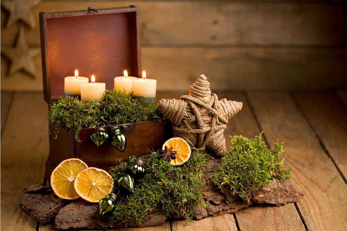 Adventsgesteck mit getrockneten Orangen, Moos, einem Stern und Kerzen in einer Truhe [Foto: AdobeStock_Petra Schueller]