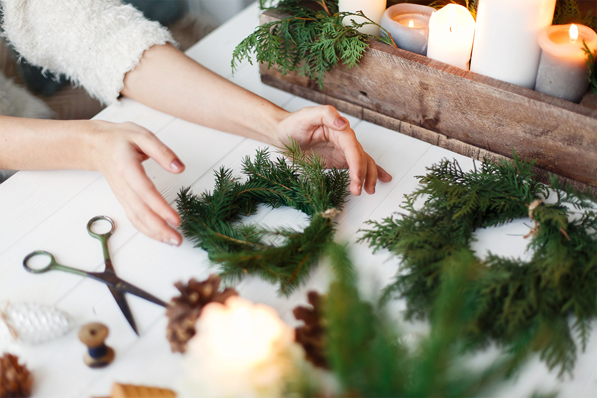 Adventsgesteck auf einem Tisch neben Bindegrün und Zapfen [Foto: AdobeStock_Sonyachny]