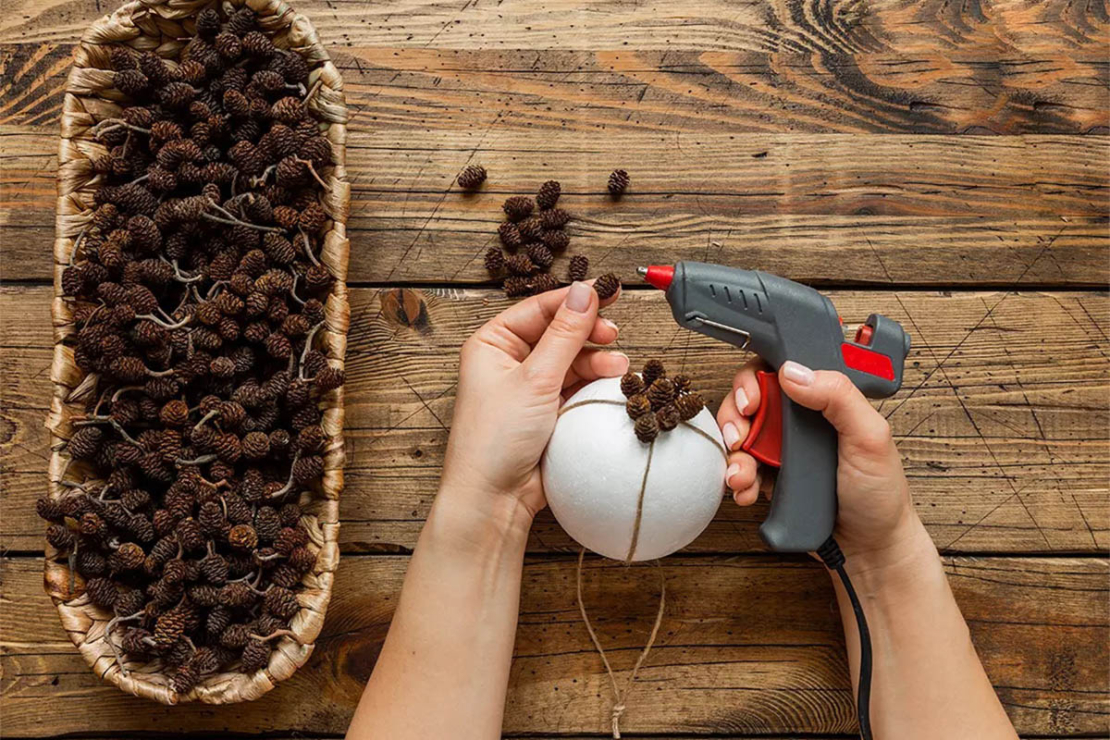 Weihnachtsbaumkugeln werden mittels Heißkleber mit kleinen Zapfen beklebt Foto: AdobeStock_Ali