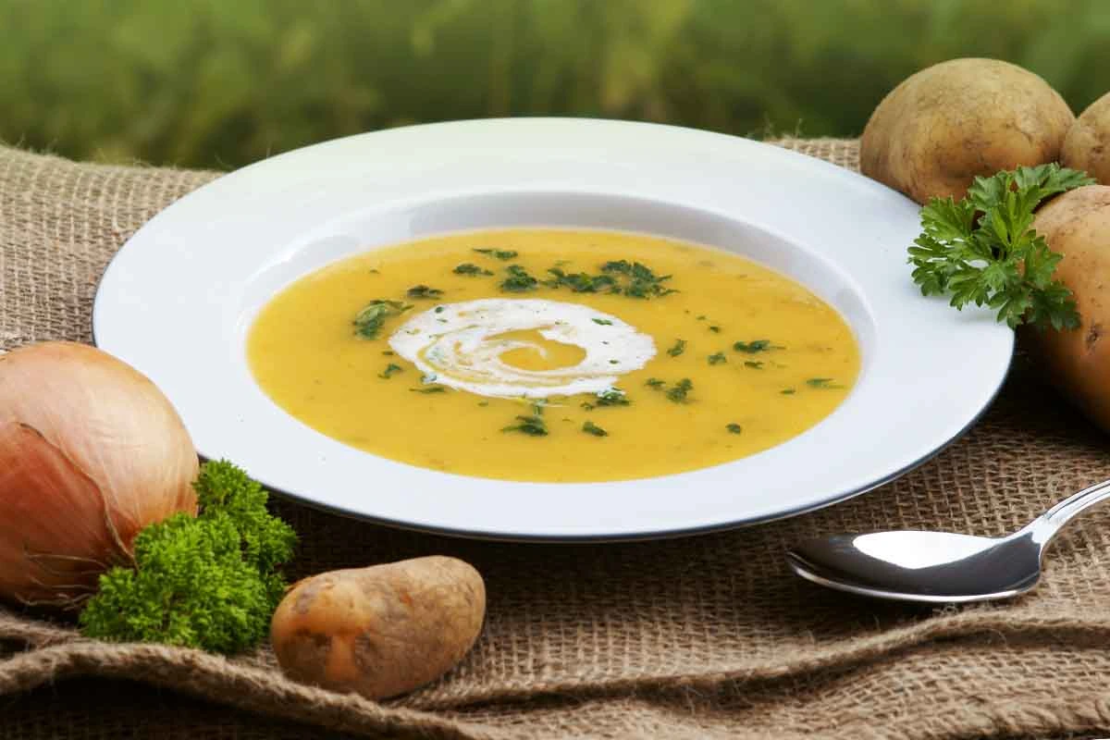 Kartoffelsuppe mit Schmand und Petersilie neben rohen Kartoffeln auf einem Gartentisch [Foto: AdobeStock_Johanna Mühlbauer]