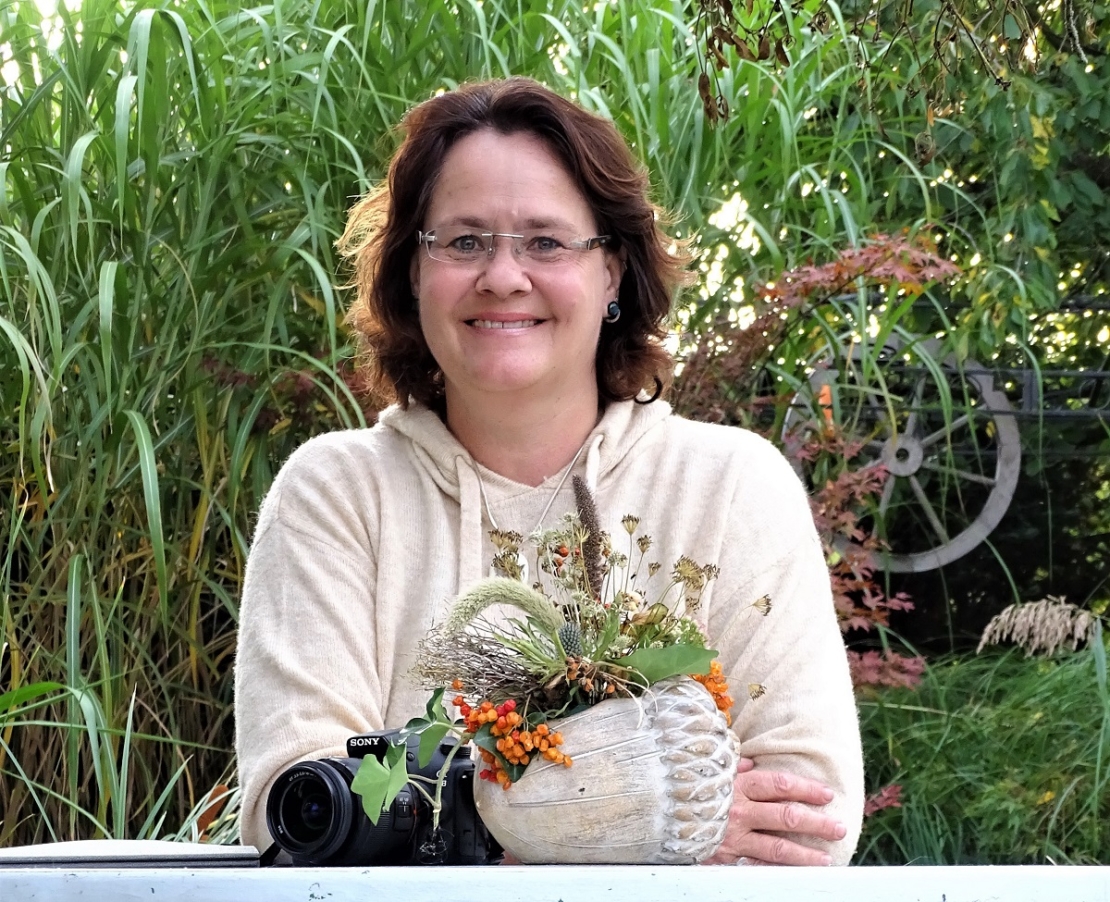 Fachredakteurin Patricia Städter sitzt im Garten am Tisch, daurauf Trockenstrauß und Kamera