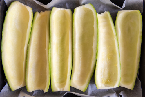 Sechs ausgehöhlte Zucchinihälften auf einem mit Backpapier ausgelegten Blech