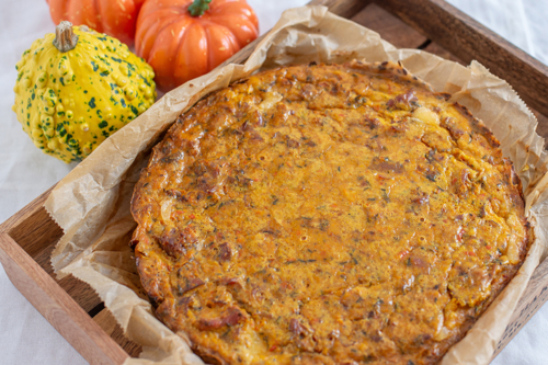 Kürbisquiche neben Kürbissen auf Holztablett