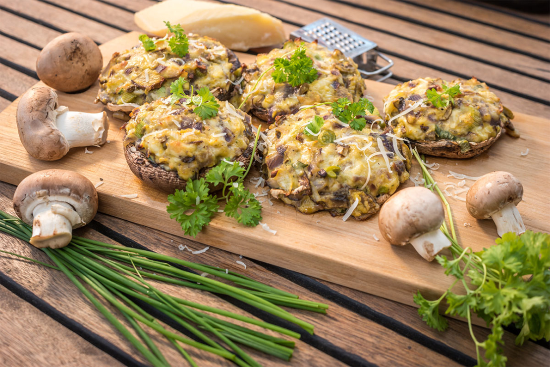 gefüllte Champignons mit Petersilie und Champignons angerichtet auf einem Holzbrettchen Foto: AdobeStock_JiriD