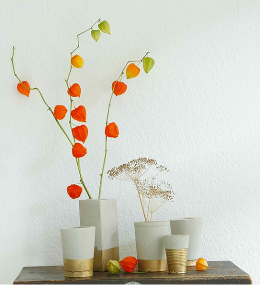 Auf Holzplatte arrangierte Vasen durch basteln mit Beton hergestellt, mit Goldspray veredelt und mit Trockenblumen bestückt