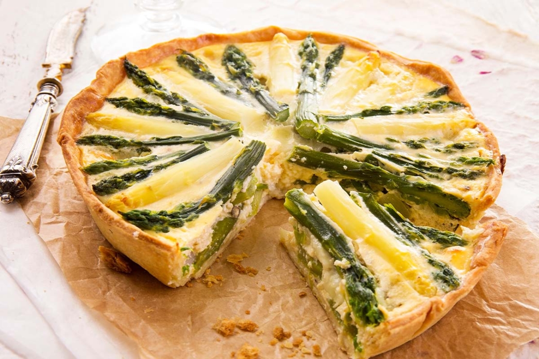 Spargelquiche wird auf Backpapier geschnitten [Foto: AdobeStock_HLPhoto]