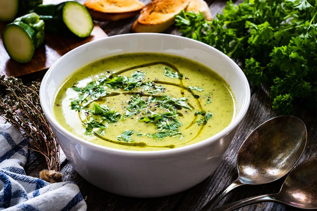 Cremige Zucchinisuppe selber machen - hier fertige Suppe in einem Schälchen auf einem Holztisch [Foto: AdobeStock_Jacek-Chabraszewski]