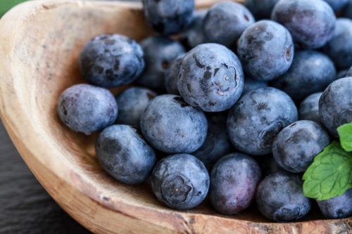 Zu sehen ist eine Holzschüssel, in der Heidelbeeren liegen.