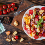 Angerichteter Tomatensalat mit gerösteten Brotwürfeln und Basilikum auf einem Holztisch