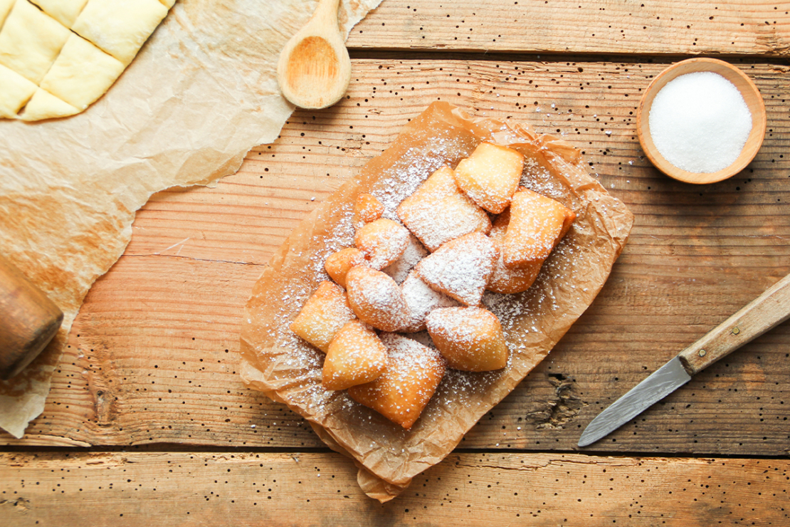 Mutzenmandeln mit Puderzucker bestreut auf einem Holztisch neben einem Holzlöffel und einem Messer [Foto: AdobeStock_Eflstudioart]