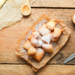 Mutzenmandeln mit Puderzucker bestreut auf einem Holztisch neben einem Holzlöffel und einem Messer [Foto: AdobeStock_Eflstudioart]