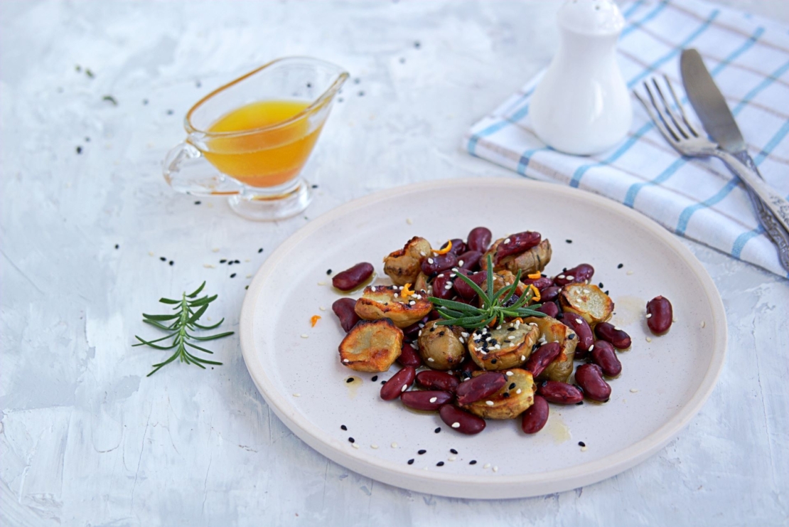 Zu sehen ist ein Teller, auf dem ein Salat aus Topinamburscheiben, Kidneybohnen und Orangenabrieb angerichtet ist.