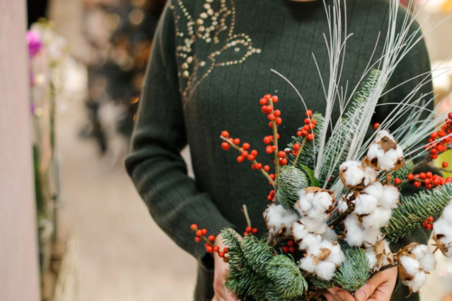 Winterlicher Blumenstrauß mit Ilex-Beeren, Tannengrün und Baumwollzweigen, den eine Frau in den Händen hält.