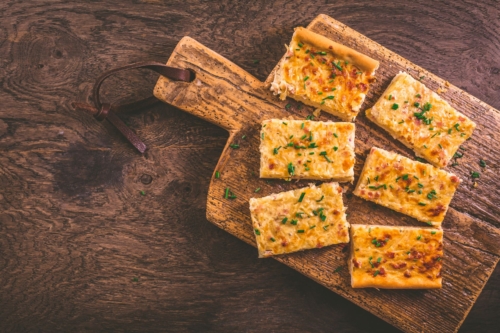 Zu sehen ist ein Holzbrett, auf dem sechs Stücke Zwiebelkuchen liegen.