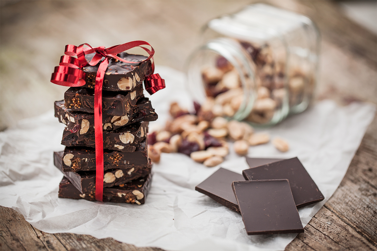 Bruchschokolade nach einem Rezept mit diversen Nüssen auf einem Tisch neben einem Glas mit Nüssen [Foto: AdobeStock_JRP Studio]