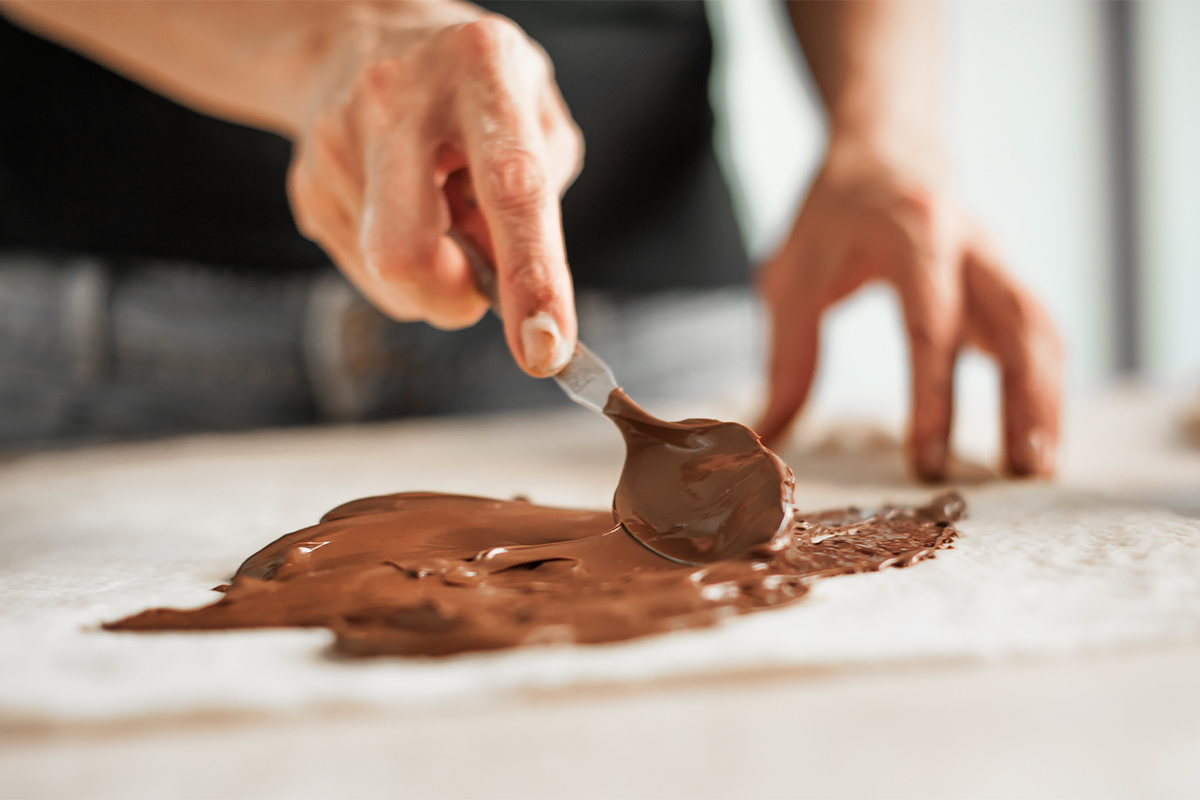 Schokolade wird mit einem Löffel auf ein Backpapier gestrichen [Foto: AdobeStock_GuruXOX]