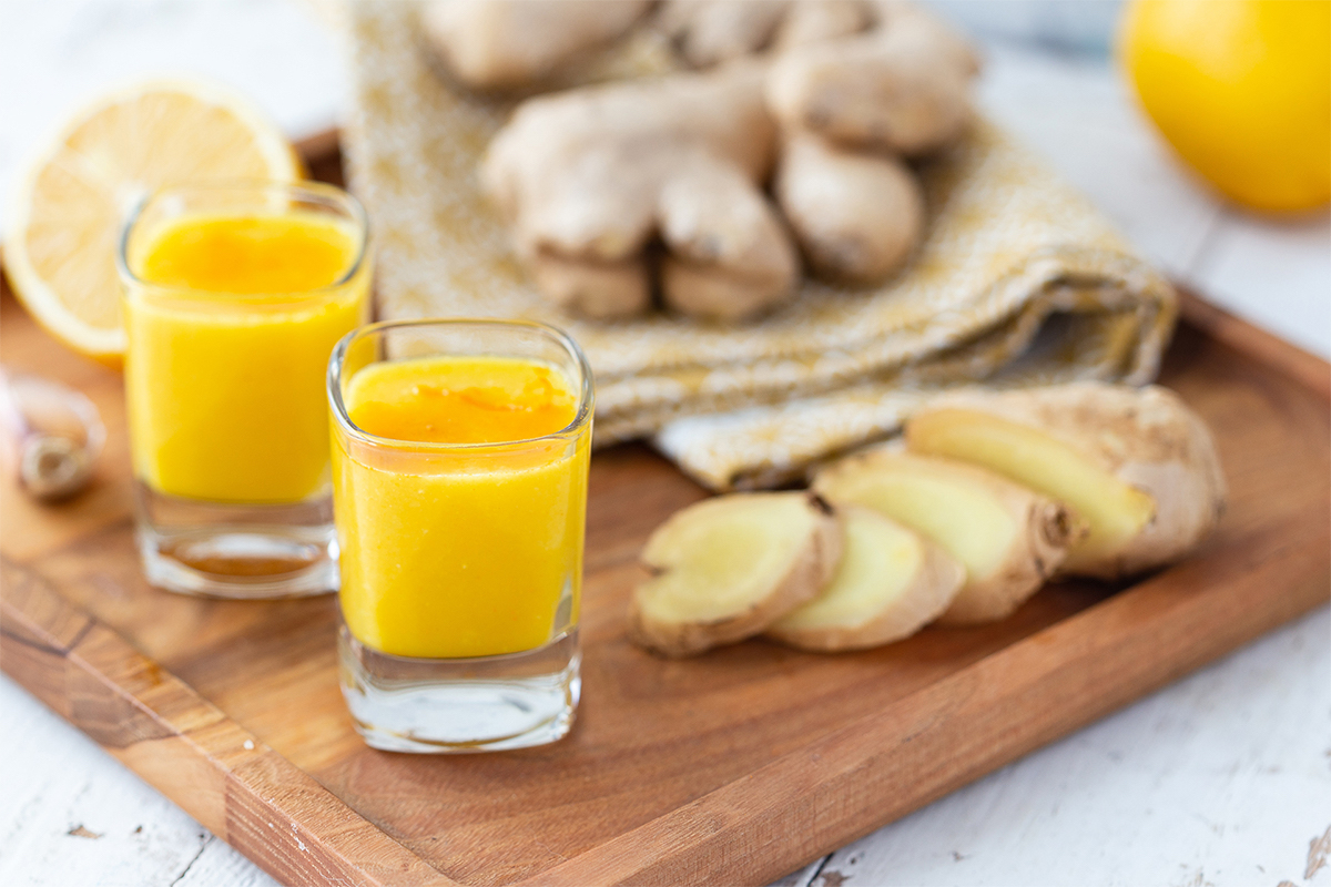 Ingwer Shot auf einem Tisch neben Ingwer und Zitrone [Foto: AdobeStock__Елена Завалко]