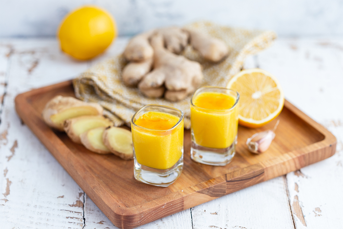 Ingwer-Shot mit Zitrone neben Zitronen und Ingwer auf einem Tisch [Foto: AdobeStock_Елена Завалко]