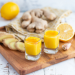 Ingwer-Shot mit Zitrone neben Zitronen und Ingwer auf einem Tisch [Foto: AdobeStock_Елена Завалко]