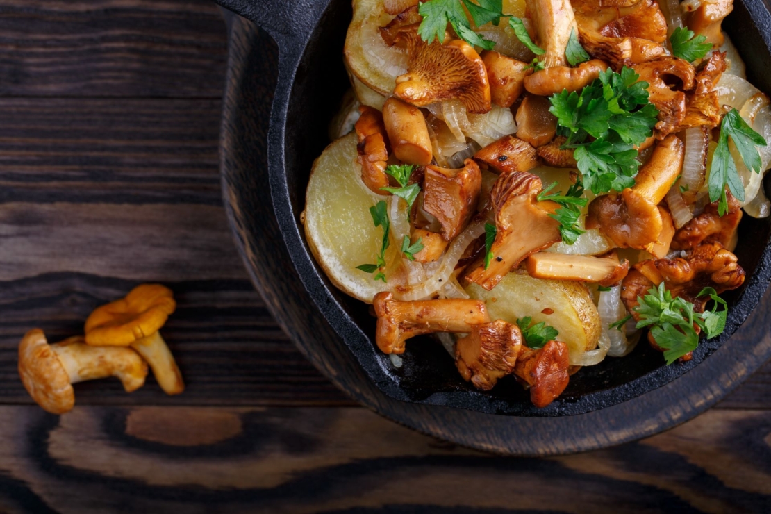 Pilzpfanne mit Kartoffeln und Petersilie in gusseiserner Pfanne auf einem Holztisch.