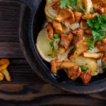 Pilzpfanne mit Kartoffeln und Petersilie in gusseiserner Pfanne auf einem Holztisch.