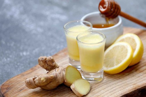 Ingwershots stehen neben Ingwer und Zitronenscheiben auf einem Holzbrettchen [Foto: AdobeStock_Oda Hoppe]