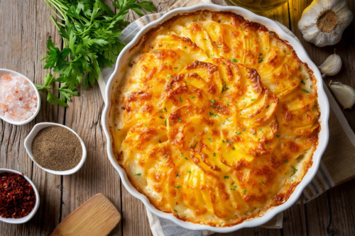 Kartoffelgratin steht in Auflaufform auf einem Holztisch [Foto: AdobeStock_Esin-Deniz]