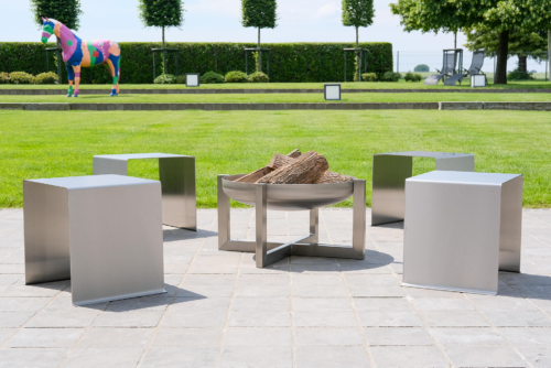 Designer-Feuerschale aus Edelstahl und dazu passende Gartenhocker in U-Form.