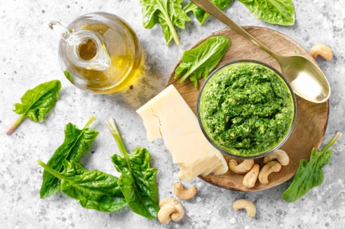 Spinatpesto in einem Glas neben Parmesan, Öl, Spinat und Cashews auf einem Tisch [Foto: AdobeStock_Sea Wave]