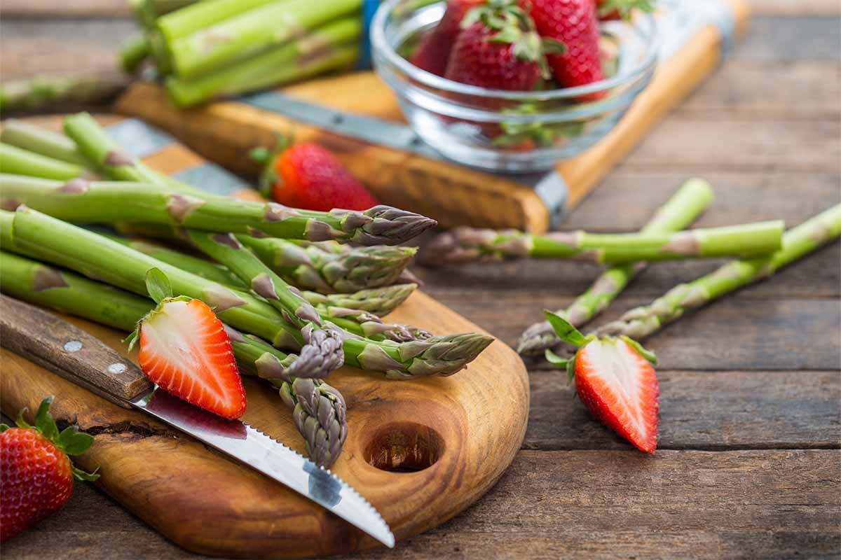 Spargel und Erdbeeren liegen fuer Spargelsalat mit Erdbeeren auf einem Holzbrett [Foto: AdobeStock_Pilipphoto]