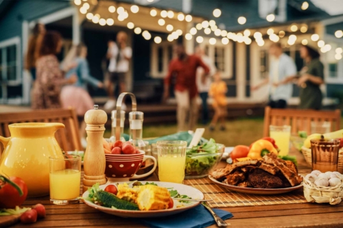 Bild von einer Grillparty mit einer gedeckten Tafel im Vordergrund und Gästen im Hintergrund [Foto: AdobeStock_Gorodenkoff]