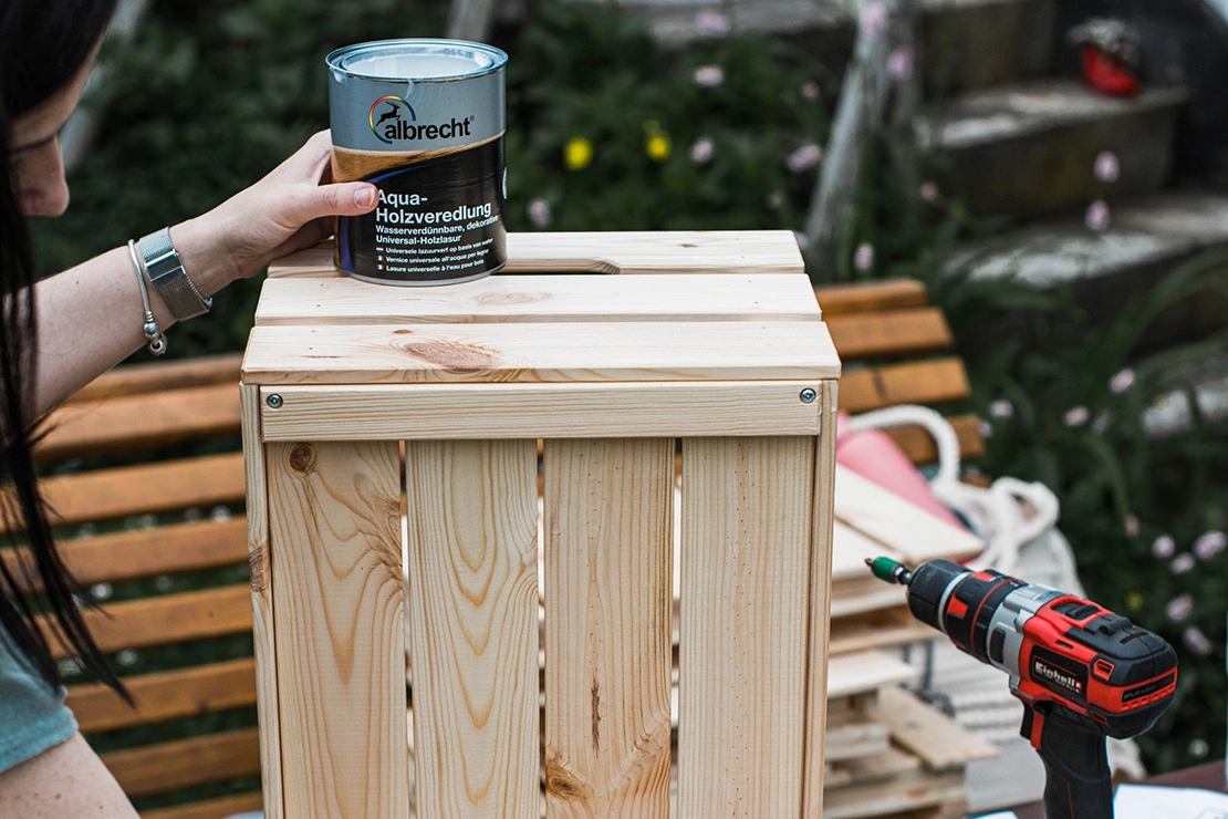 Eine unbehandelte Holzkiste wird mit einer Lasur bearbeitet. Foto: Einhell