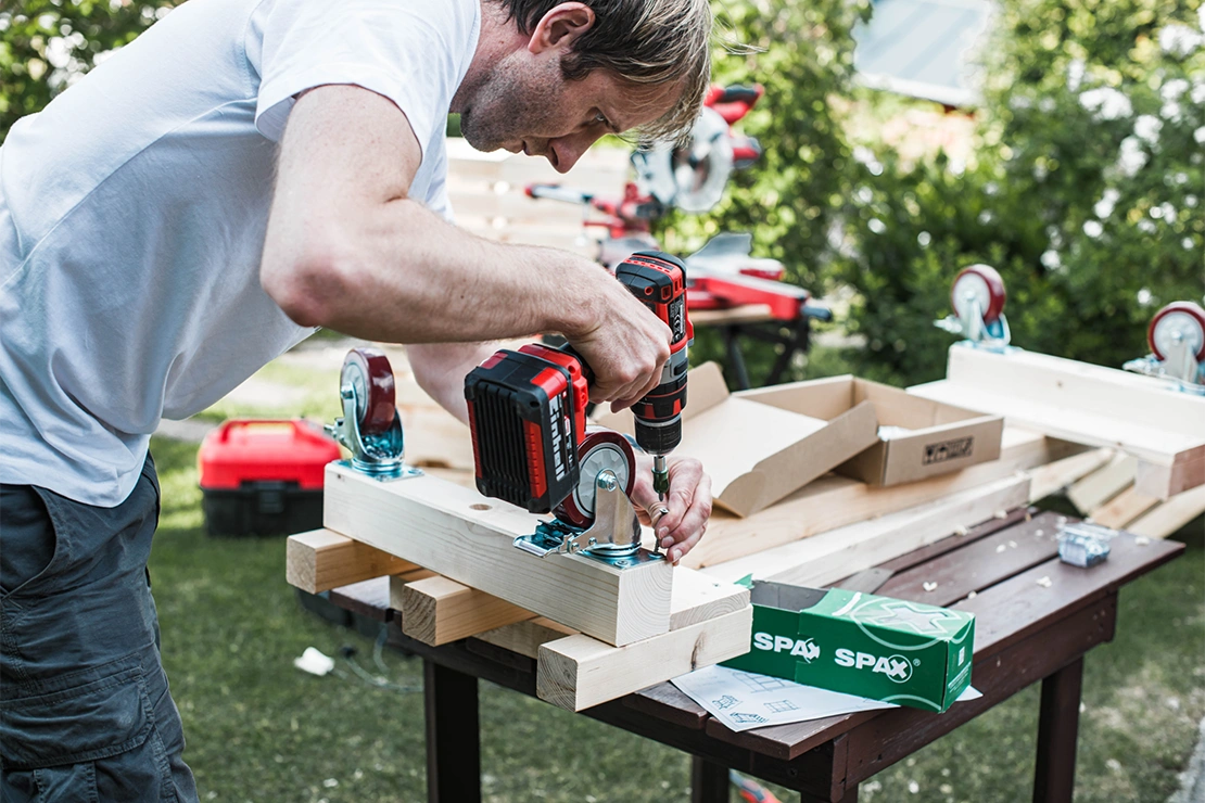 Ein Mann verschraubt Hölzer für eine Outdoor-Bar im Garten. Foto: Einhell