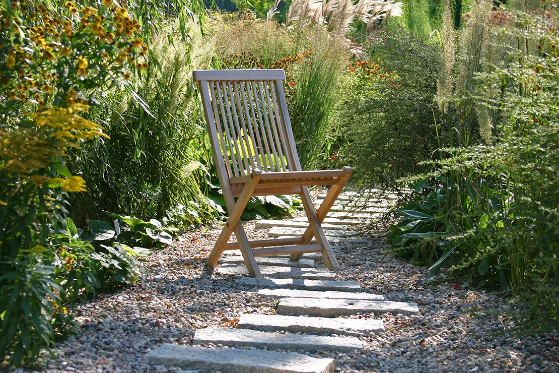 Unkrautvlies: Ein Holzstuhl steht auf einem Kiesweg im Garten. Foto: AdobeStock_spuno