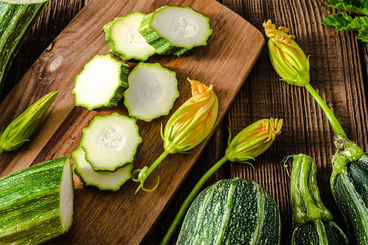 Zucchinischeiben neben Zucchini und Blueten fuer eine Zucchinisuppe [Foto: AdobeStock_Alicja Neumiler]