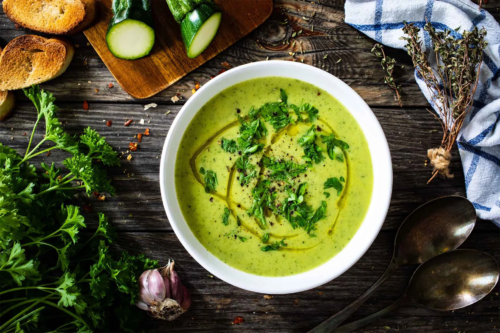 Zucchinisuppe von oben fotografiert – daneben liegen Zucchini und andere Zutaten [Foto: AdobeStock_Jacek Chabraszewski]