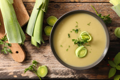 Lauchsuppe neben Porree und einem Schneidebrett auf Holztisch [Foto: AdobeStock_M.studio.]